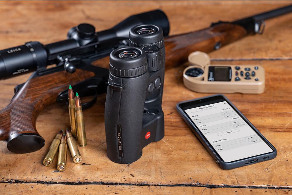 Leica Ballistics App shown on the phone with a rifle in the background and a Geovid Pro on the side